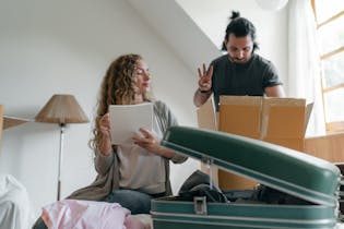 A couple happily packs boxes in their bright, cozy bedroom, preparing for a move.